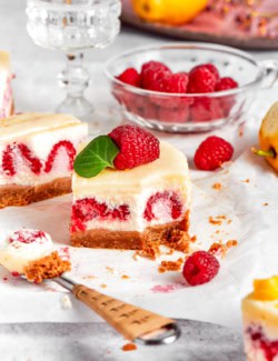 a lemon cheesecake bar with fresh raspberries, with a forkful removed