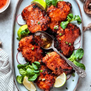 lemongrass chicken thighs on a platter with lime wedges and fresh greens