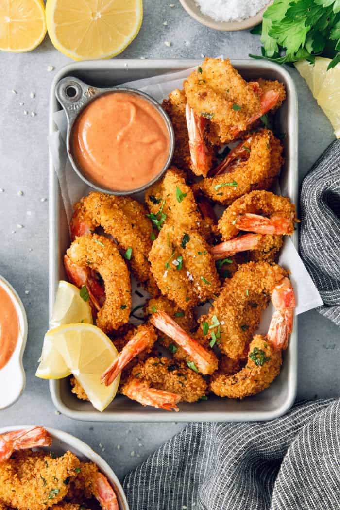 Crispy butterfly shrimp in metal tray with cocktail sauce and lemon wedges
