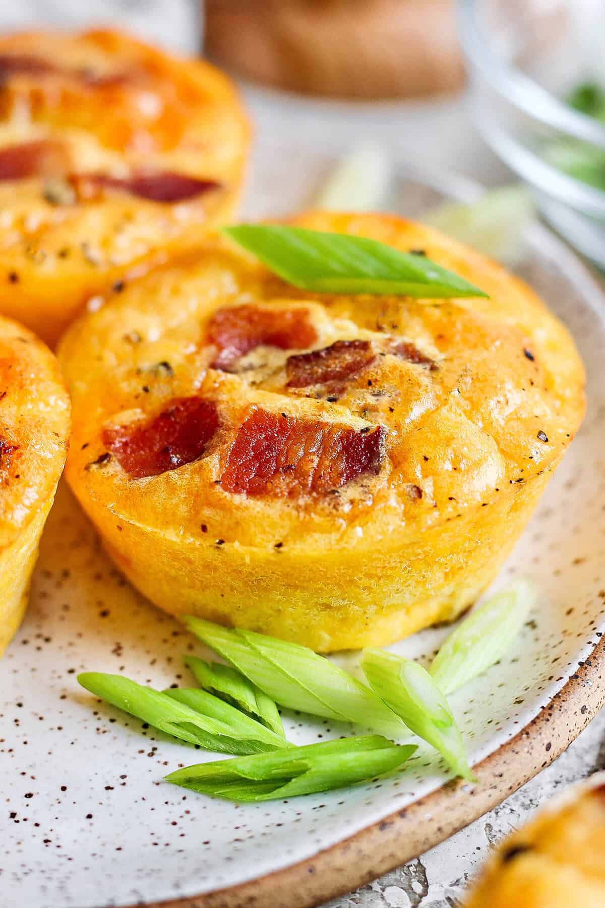 Cottage Cheese Egg Bites are creamy, cheesy and packed with protein. And let’s not forget the bacon! The perfect savory meal prep breakfast. Closeup of cottage cheese egg bite on plate with green onions for garnish