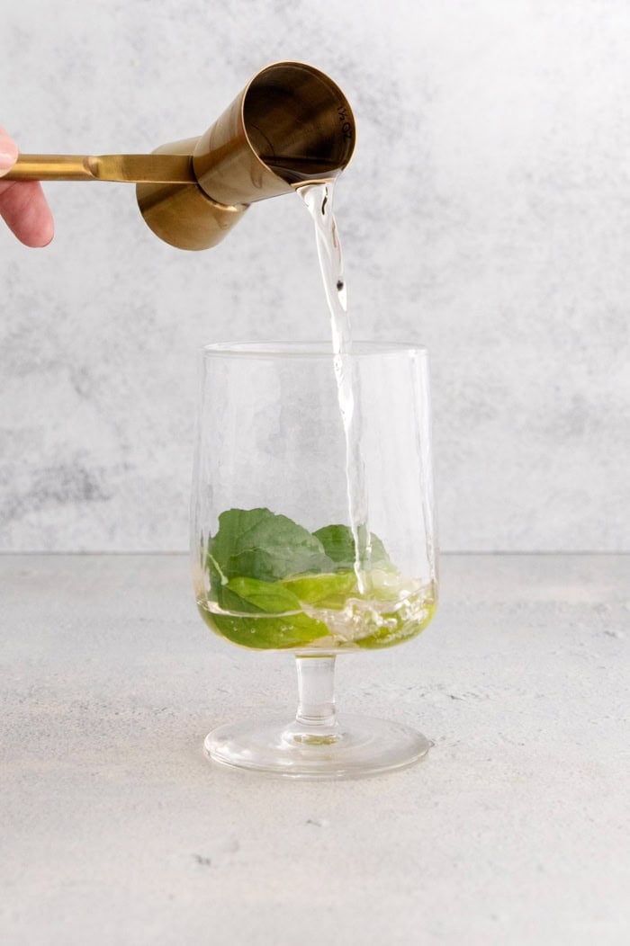 Pouring St-Germain into glass with lime wheels and mint