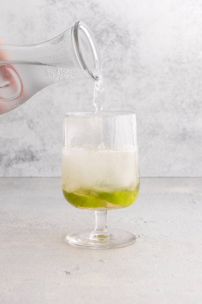 Pouring club soda into glass for Hugo spritz
