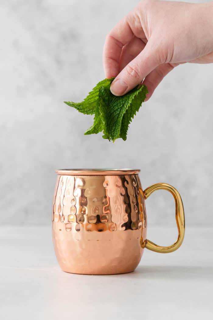 Hand placing mint leaves in copper mug