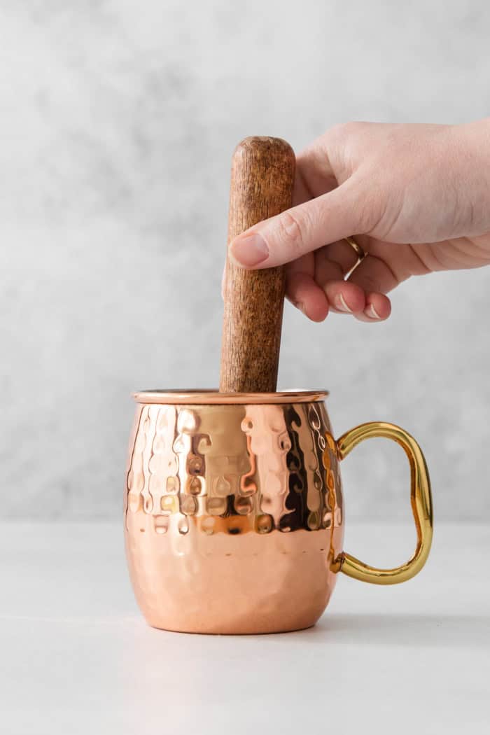 Muddling ingredients in copper Moscow mule mug