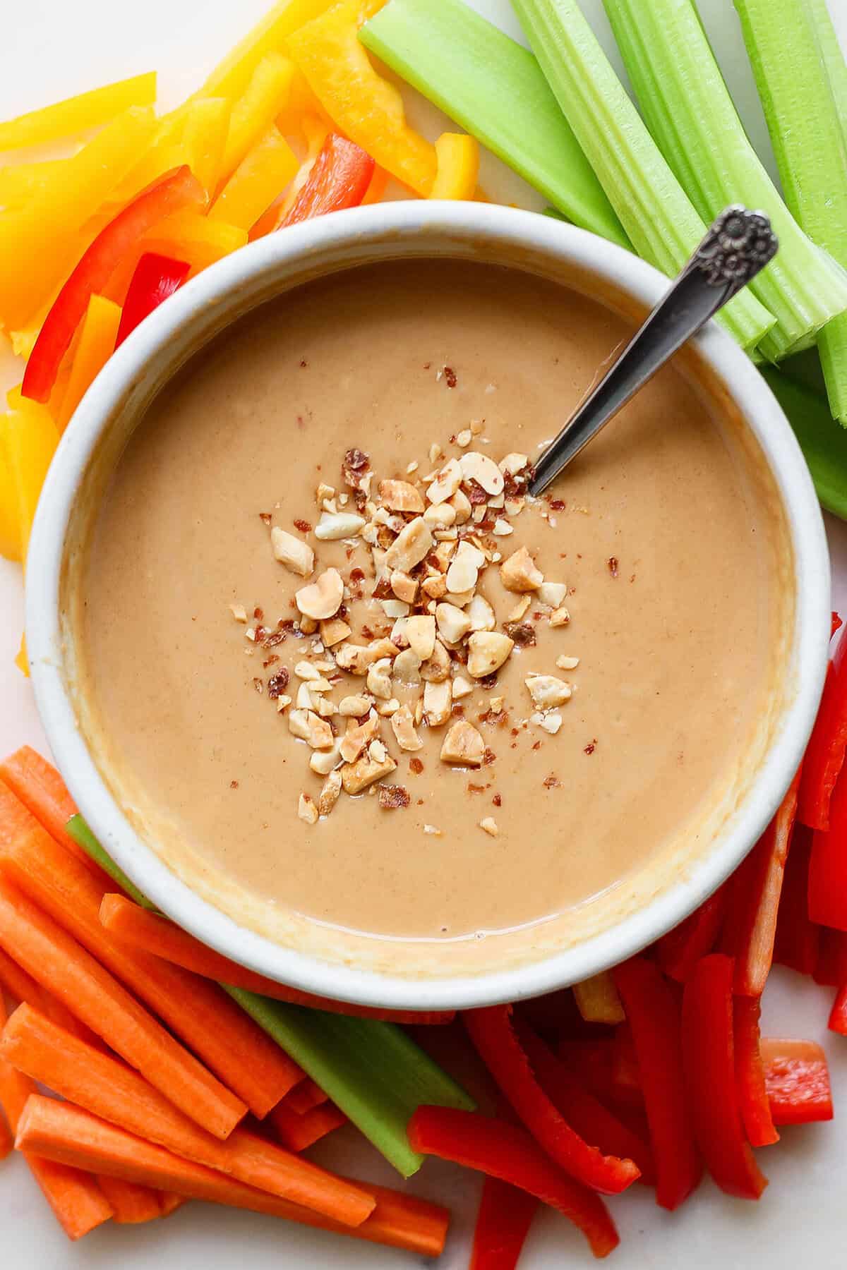 Overhead view of peanut sauce in bowl with spoon, on platter of fresh vegetables for dipping