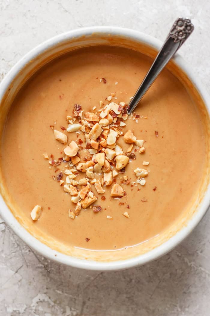 Spoon in bowl of homemade peanut sauce with chopped peanuts for garnish