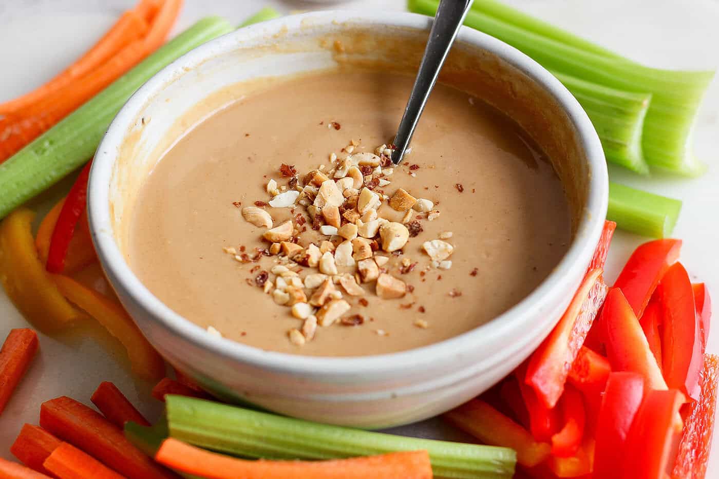 Bowl of peanut sauce topped with chopped peanuts, surrounded by crudite