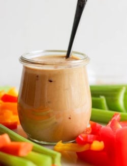 Jar of peanut sauce with spoon, surrounded by crudites