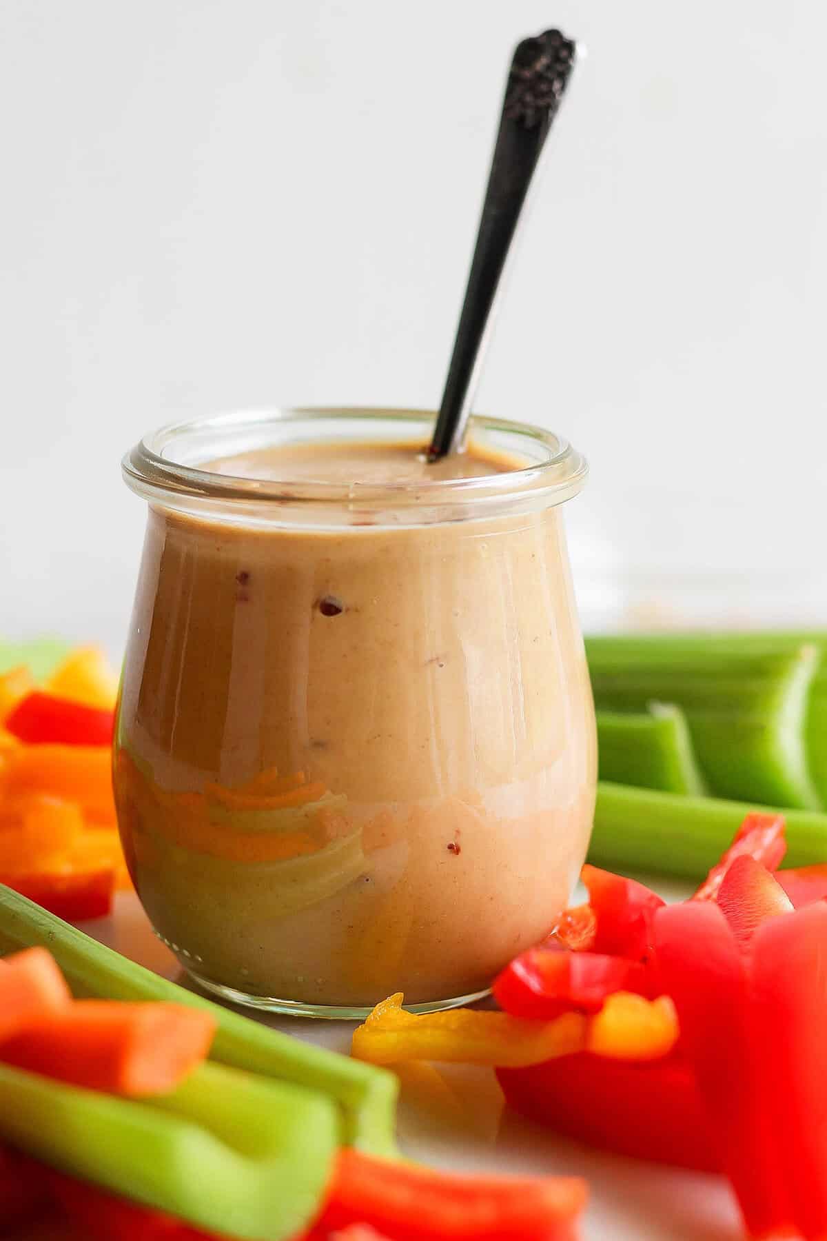 This homemade peanut sauce is creamy and sweet, but also tangy, garlicky, and just a little bit spicy. But best of all, it's SO easy to make! Jar of peanut sauce with spoon, surrounded by crudites