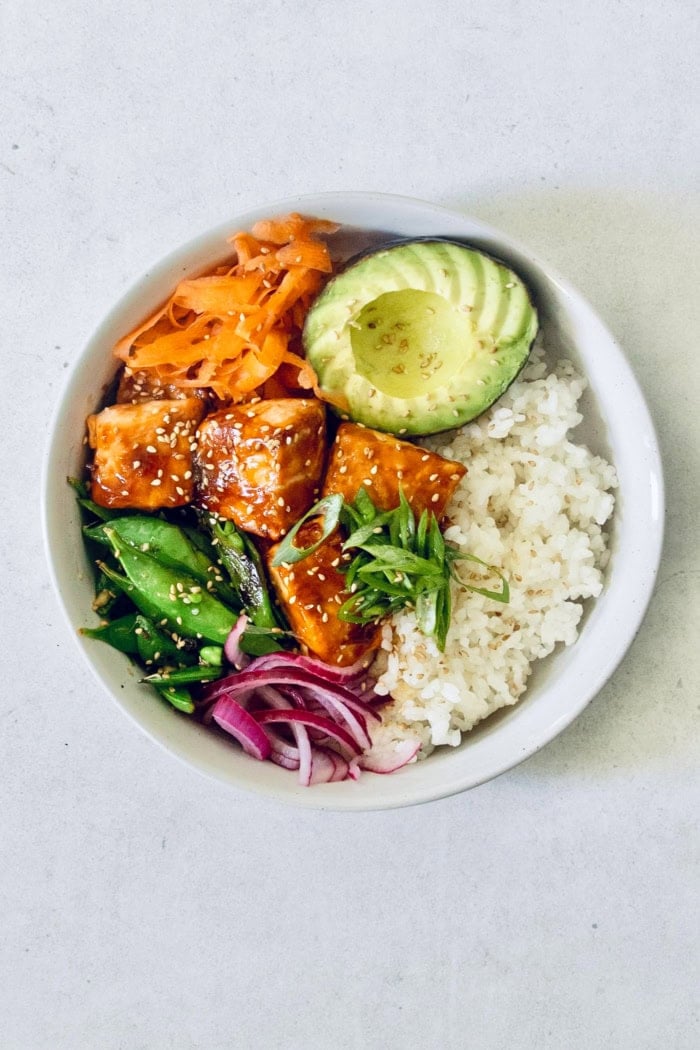Overhead view of teriyaki salmon bowl with avocado, carrots, snap peas, and rice