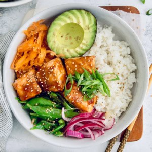 Overhead view of teriyaki salmon bowl with avocado, carrots, snap peas, and rice