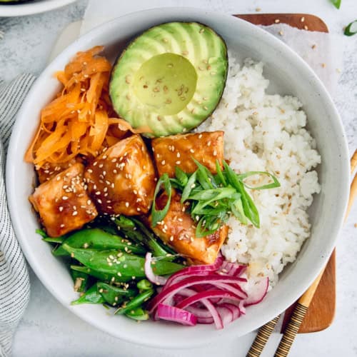 Overhead view of teriyaki salmon bowl with avocado, carrots, snap peas, and rice