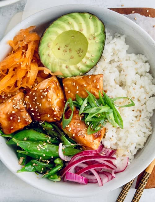 Overhead view of teriyaki salmon bowl with avocado, carrots, snap peas, and rice