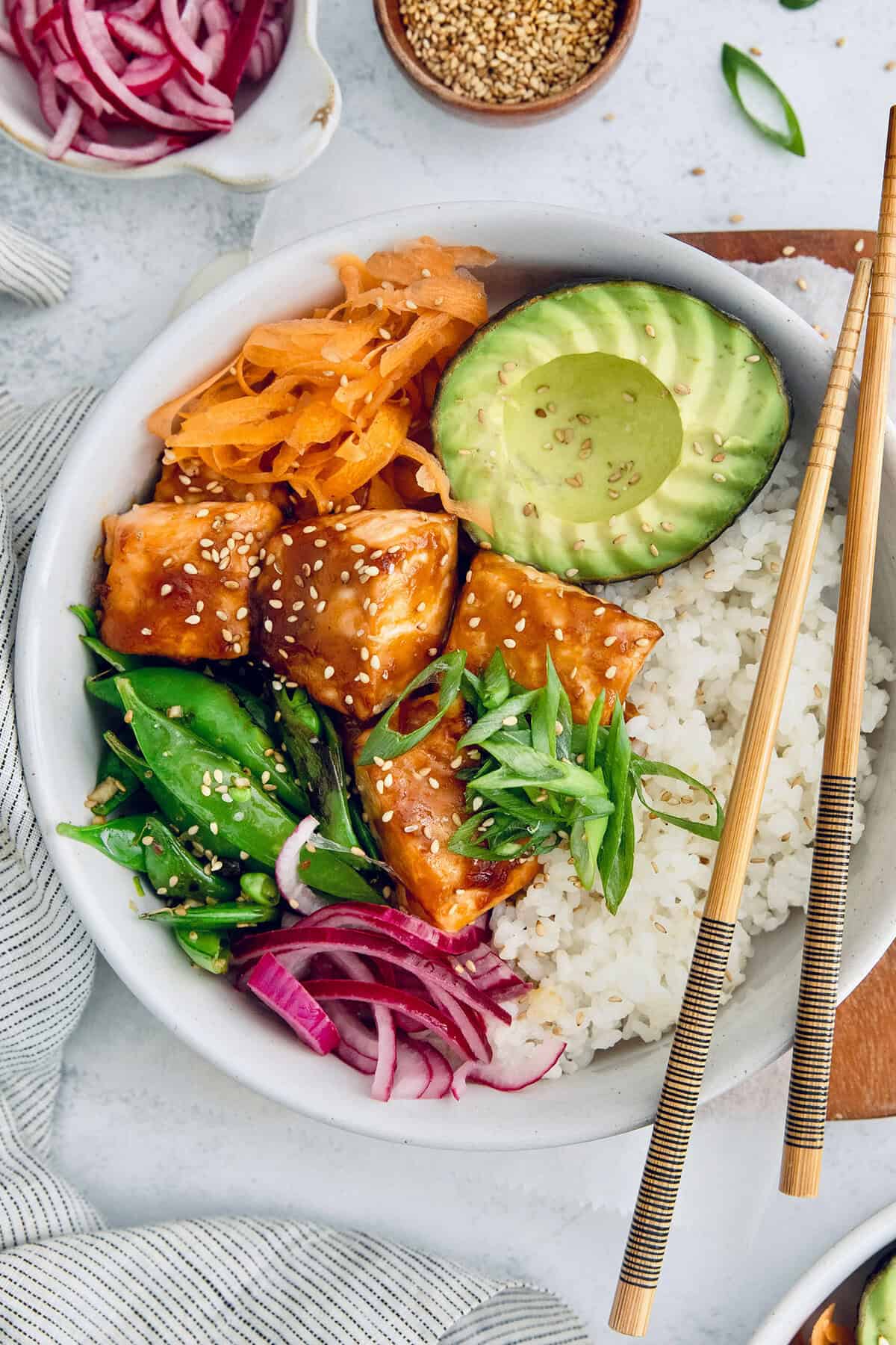 Overhead view of teriyaki salmon bowl with avocado, carrots, snap peas, and rice