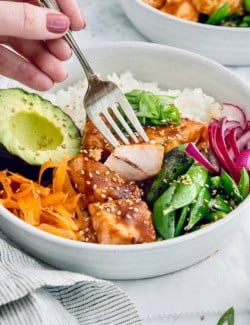 Fork piercing teriyaki salmon bite in meal bowl