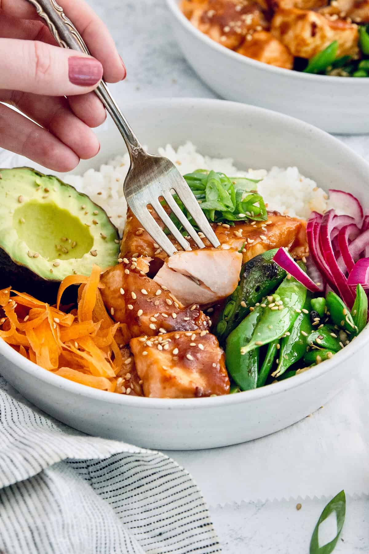 Fork piercing teriyaki salmon bite in meal bowl