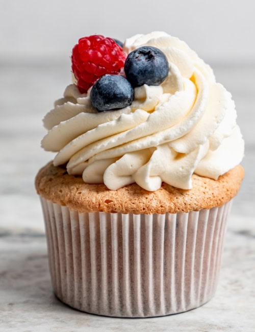 an angel food cupcake topped with white frosting and fresh berries