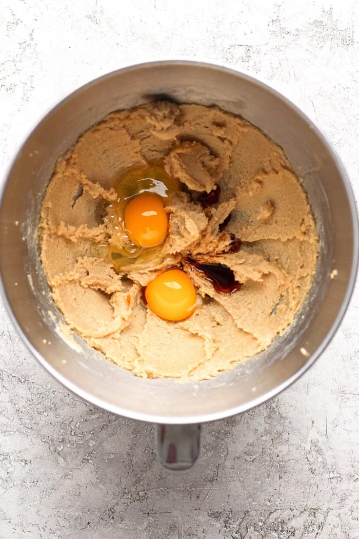 Egg and egg yolk cracked into bowl with vanilla and creamed butter and sugar