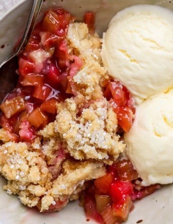 Overhead view of rhubarb dump cake in bowl with spoon and scoops of vanilla ice cream