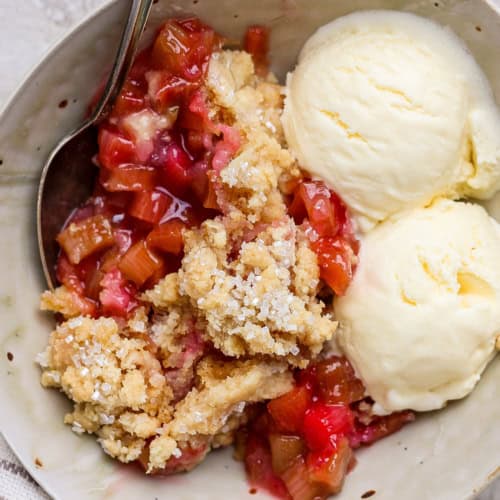 Overhead view of rhubarb dump cake in bowl with spoon and scoops of vanilla ice cream