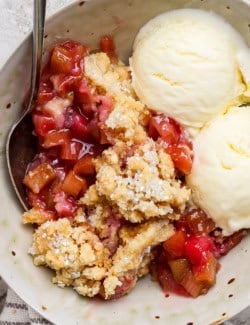 Overhead view of rhubarb dump cake in bowl with spoon and scoops of vanilla ice cream