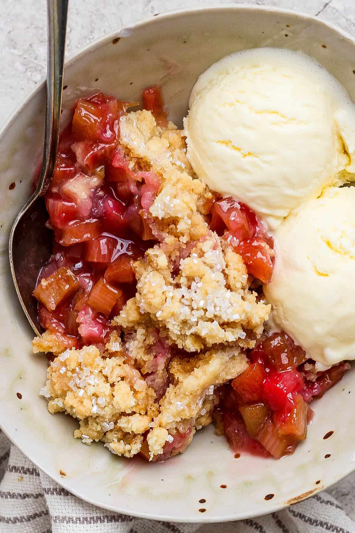 Tart, puckery rhubarb is the star of this easy rhubarb dump cake recipe, which transforms vanilla cake mix into a truly special dessert! Overhead view of rhubarb dump cake in bowl with spoon and scoops of vanilla ice cream
