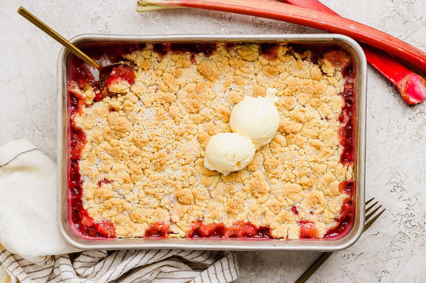 Overhead view of rhubarb dump cake in pan with spoon and two scoops of vanilla ice cream on top