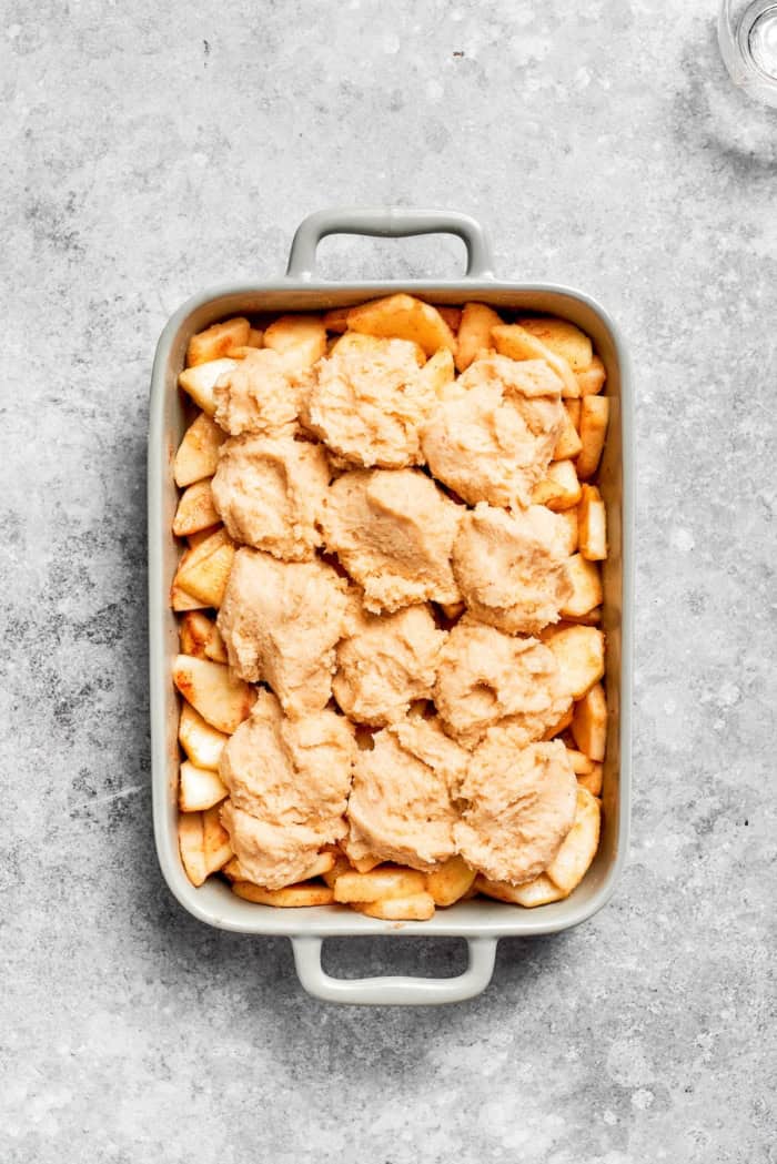 Apple Cobbler has apple pie flavor in an easier form, swapping the crust for a biscuit-like topping that bakes up tender and golden brown! Overhead view of apple cobbler in baking dish before baking