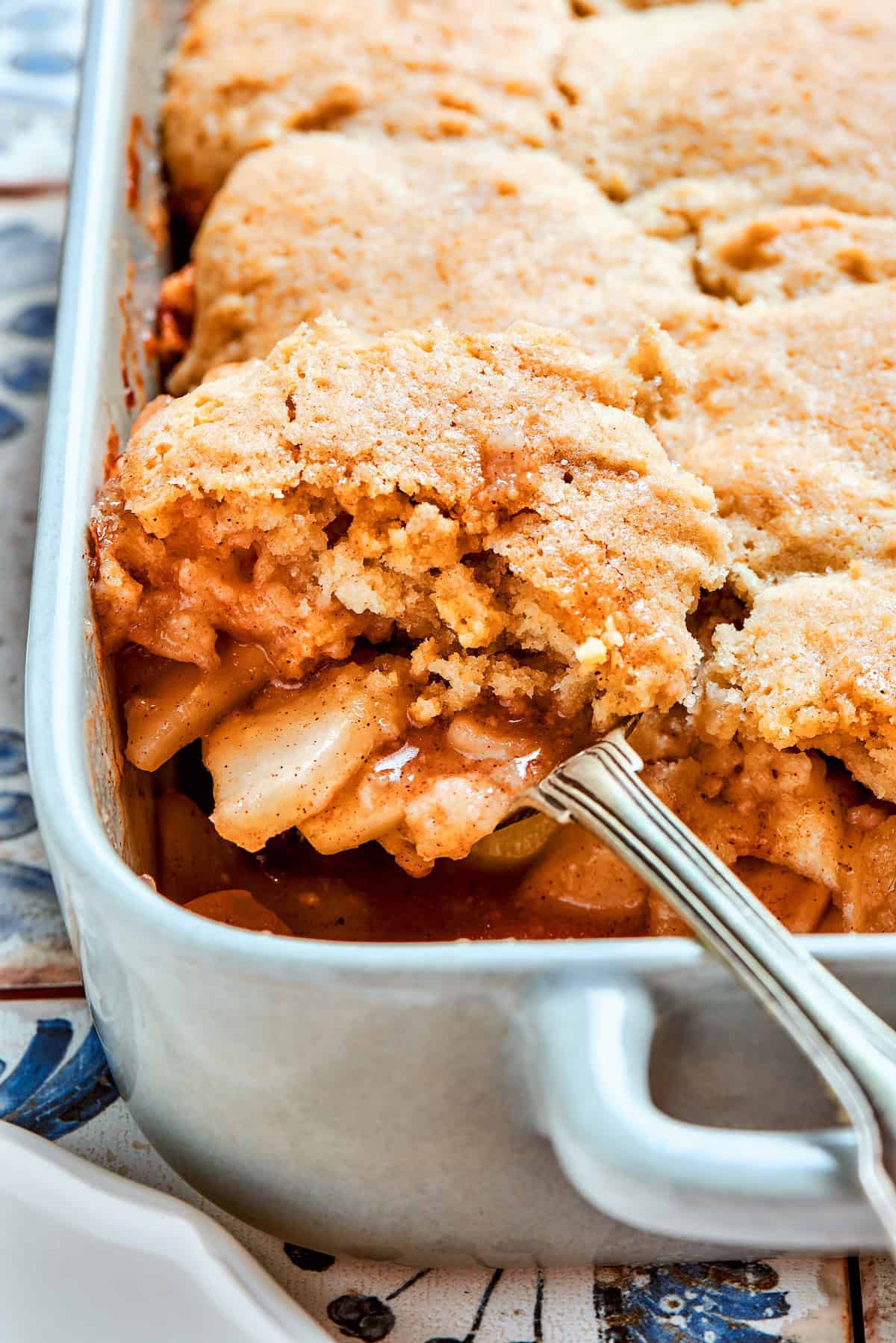 Apple Cobbler has apple pie flavor in an easier form, swapping the crust for a biscuit-like topping that bakes up tender and golden brown! Spoon scooping out portion of apple cobbler