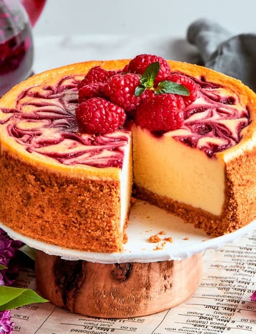 Raspberry cheesecake on a platter, with a piece removed