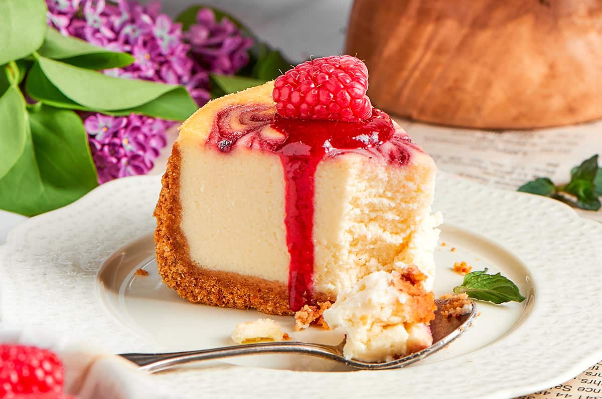 This rich raspberry cheesecake is sure to make your all-time-favorites list. It's rich, creamy, and elegant, but surprisingly easy to make! a piece of raspberry cheesecake on a white plate, with a spoonful removed