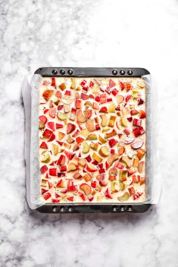 Buttery shortbread is layered with rhubarb custard to create these irresistible Rhubarb Custard Bars. Don't skip the cream cheese topping! Overhead view of rhubarb bars in pan before baking