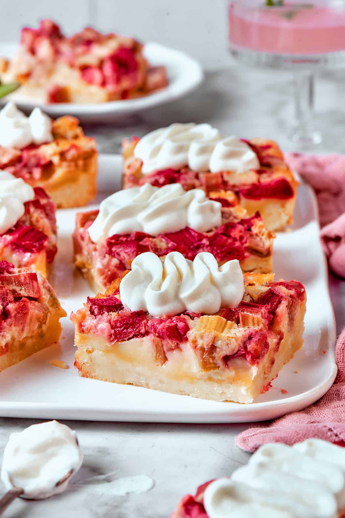 Buttery shortbread is layered with rhubarb custard to create these irresistible Rhubarb Custard Bars. Don't skip the cream cheese topping! rhubarb custard bars with cream cheese topping, on a white platter