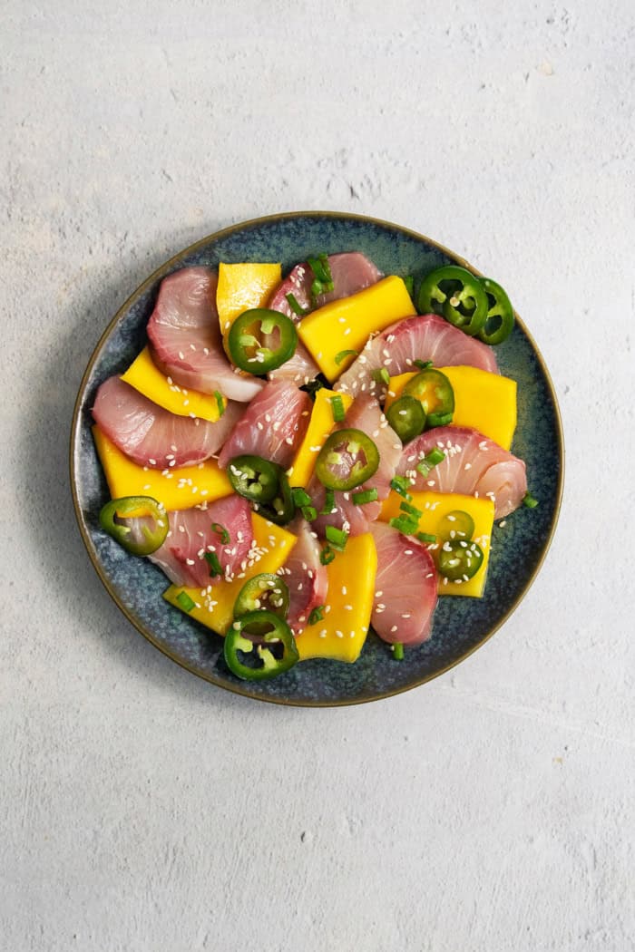 Overhead view of hamachi crudo on plate with mango and pickled jalapeno