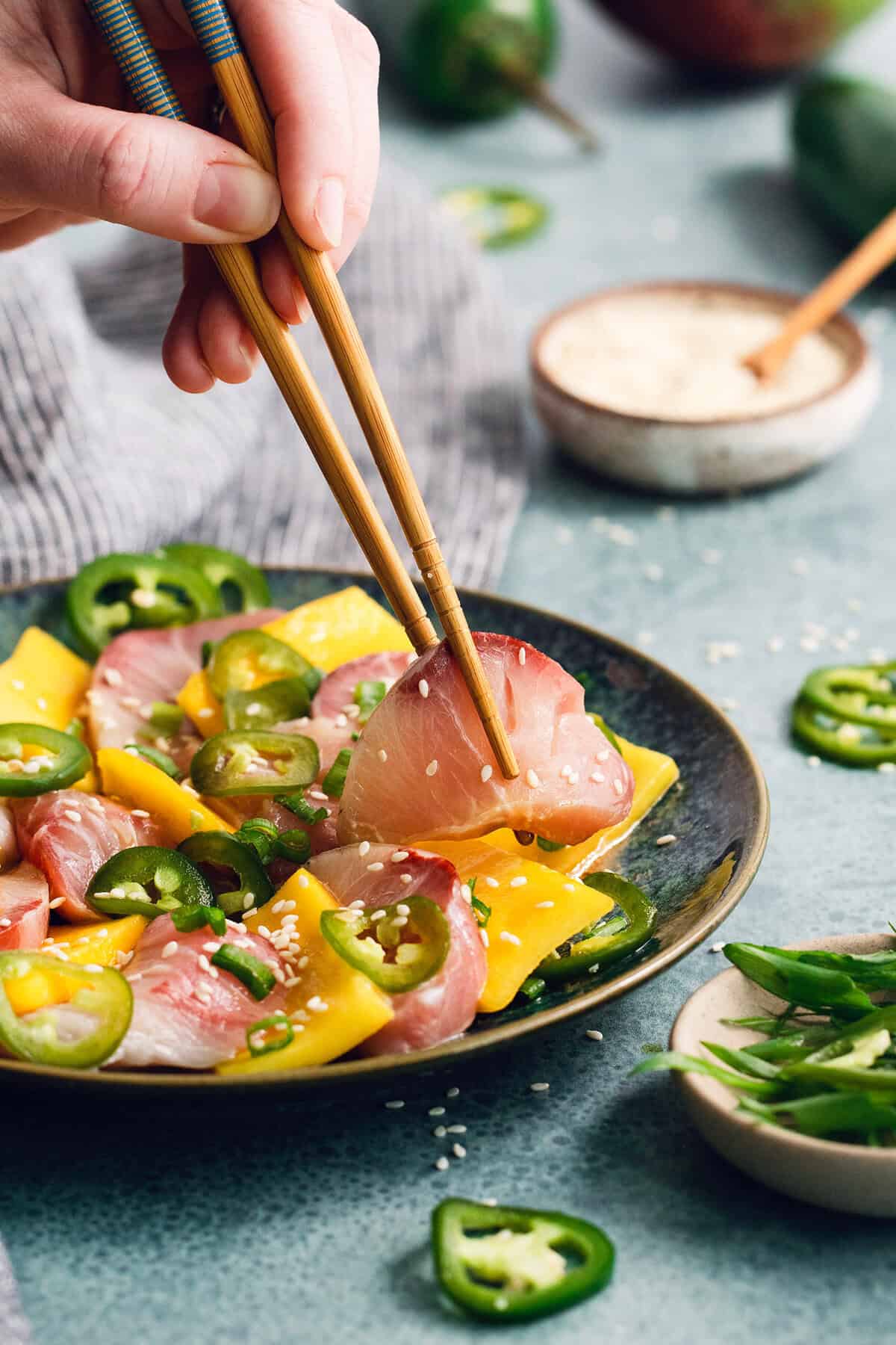 Chopsticks lifting hamachi crudo from plate