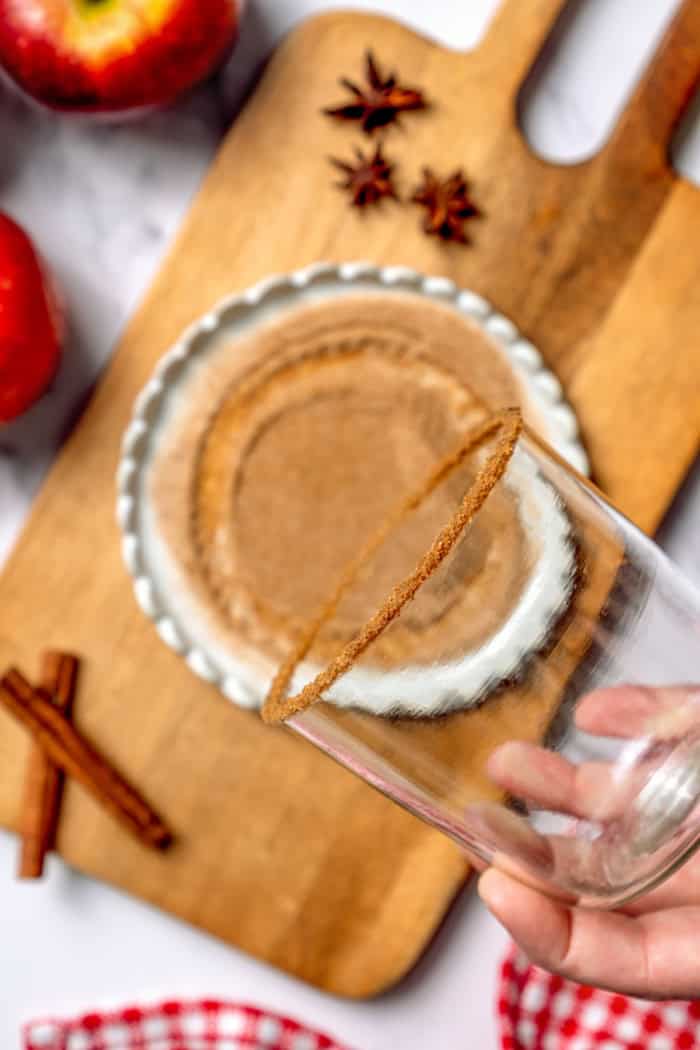 A fall spin on the classic, this Apple Cider Margarita is lightly sweetened with maple syrup and a cinnamon rim add a festive touch! Hand holding rimmed glass for margarita.