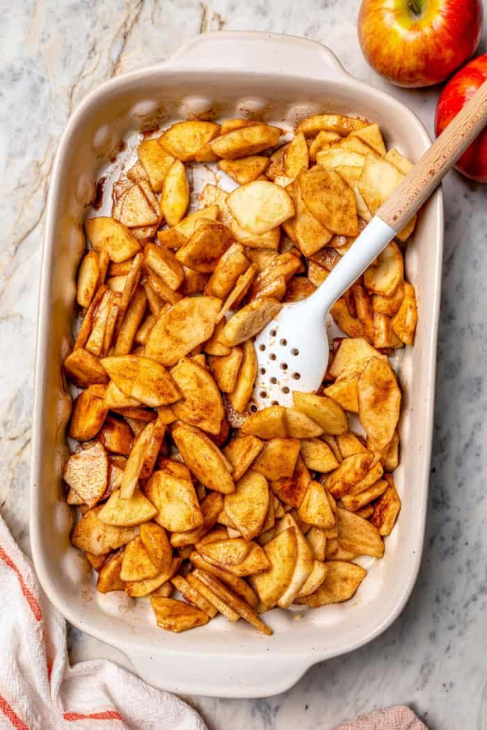 Seasoned apples in baking dish with spoon.