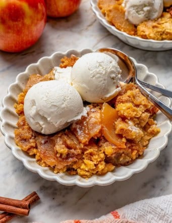 Apple dump cake in bowl with vanilla ice cream and two spoons.