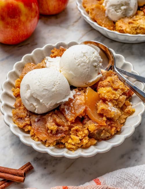Apple dump cake in bowl with vanilla ice cream and two spoons.