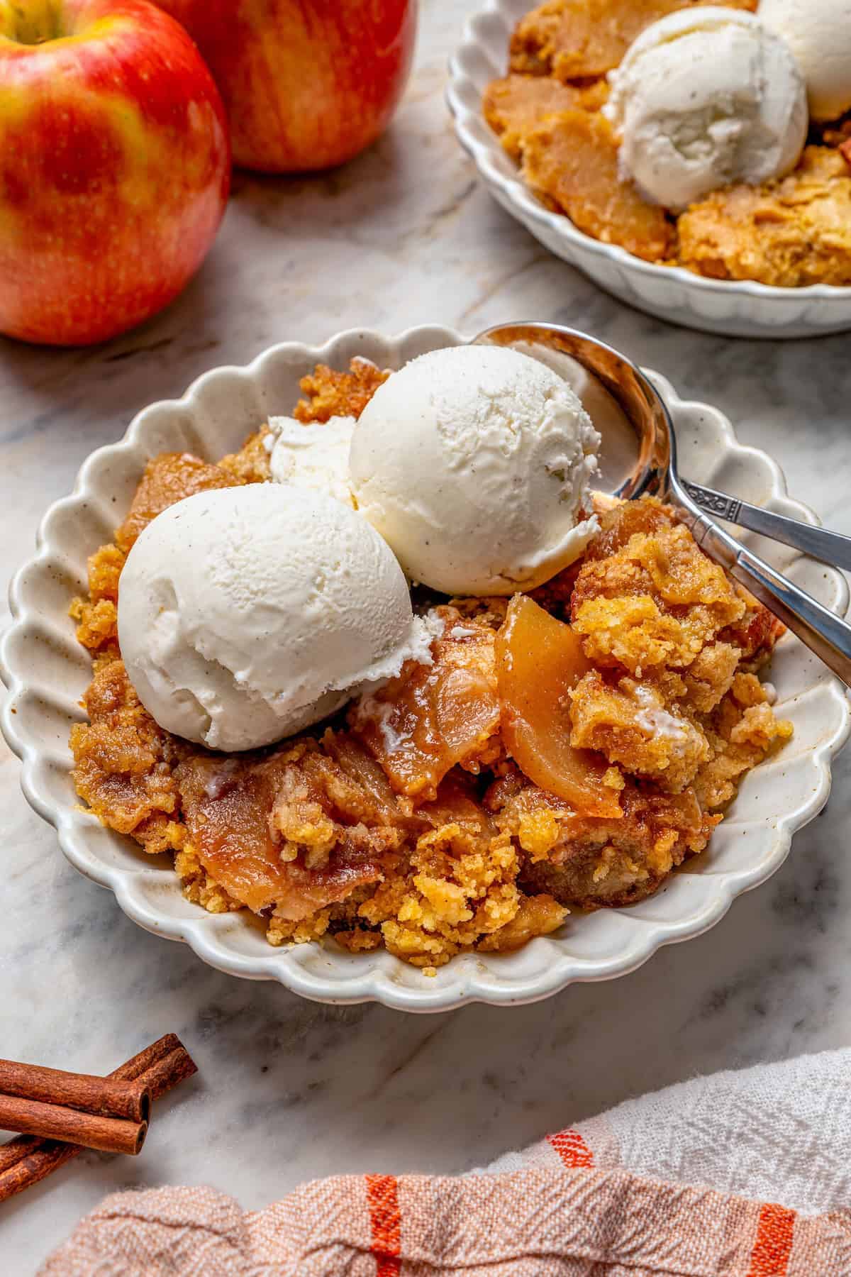 Apple dump cake in bowl with vanilla ice cream and two spoons.