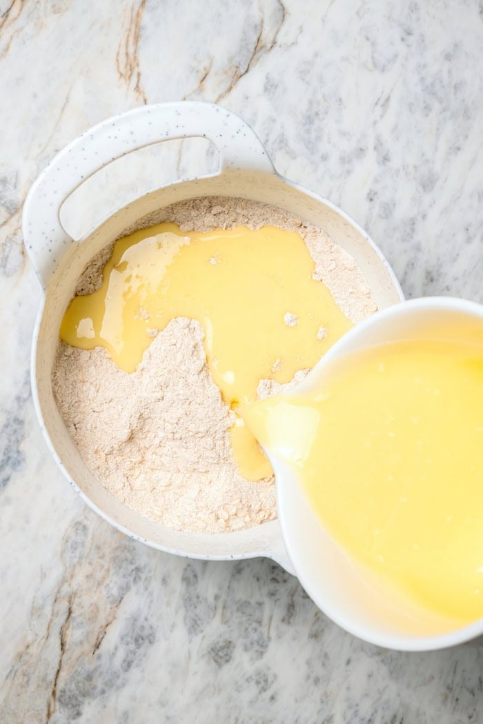 A brown sugar oat crumble mixture doubles as a crust and a topping for these easy Apple Pie Bars. The perfect fall treat for a crowd! Pouring liquid ingredients into dry ingredients for apple pie bars.