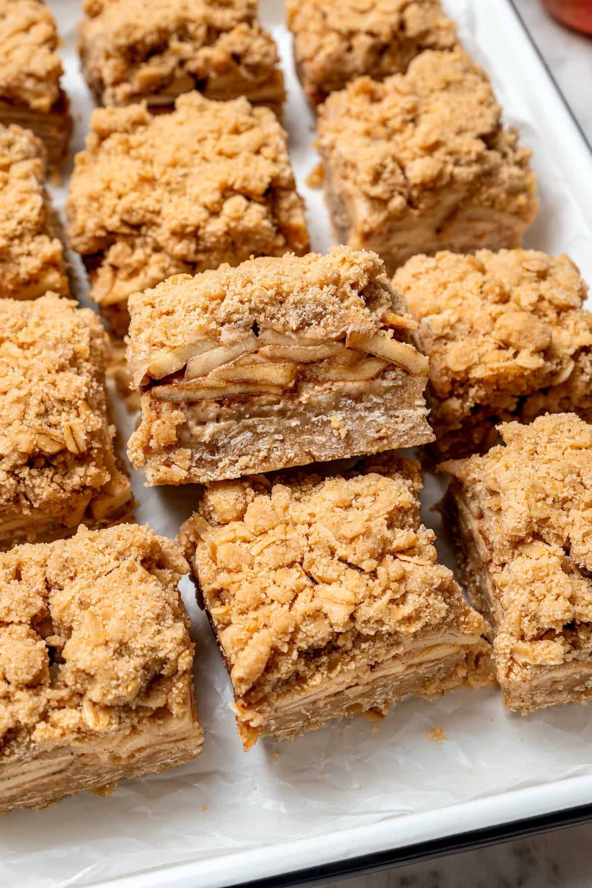 A brown sugar oat crumble mixture doubles as a crust and a topping for these easy Apple Pie Bars. The perfect fall treat for a crowd! Apple pie bars on platter with one on its side to show layers of texture.
