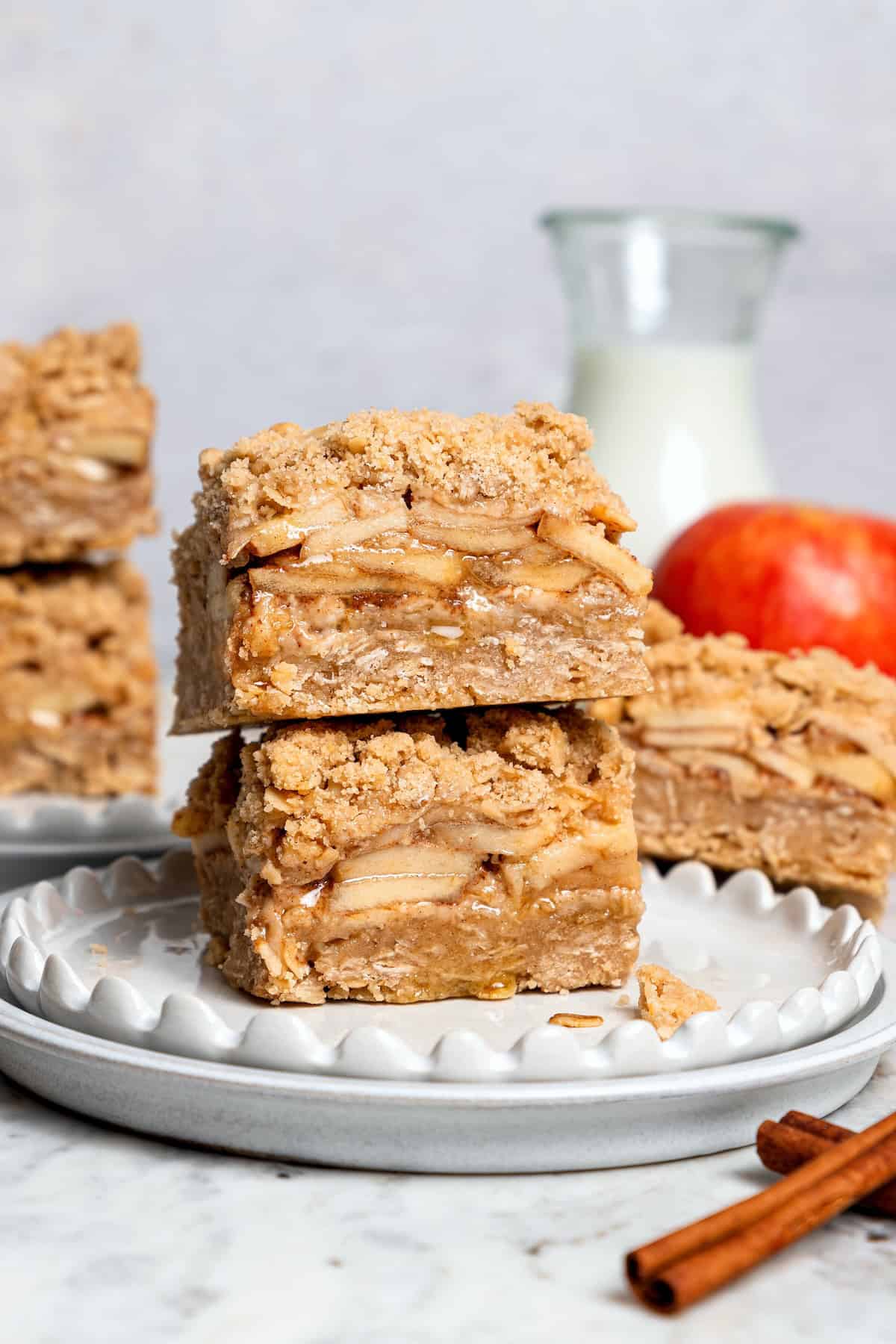 A brown sugar oat crumble mixture doubles as a crust and a topping for these easy Apple Pie Bars. The perfect fall treat for a crowd! Stack of 2 apple pie bars on plate.