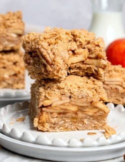 Two apple pie bars stacked on plate, with top bar bitten into