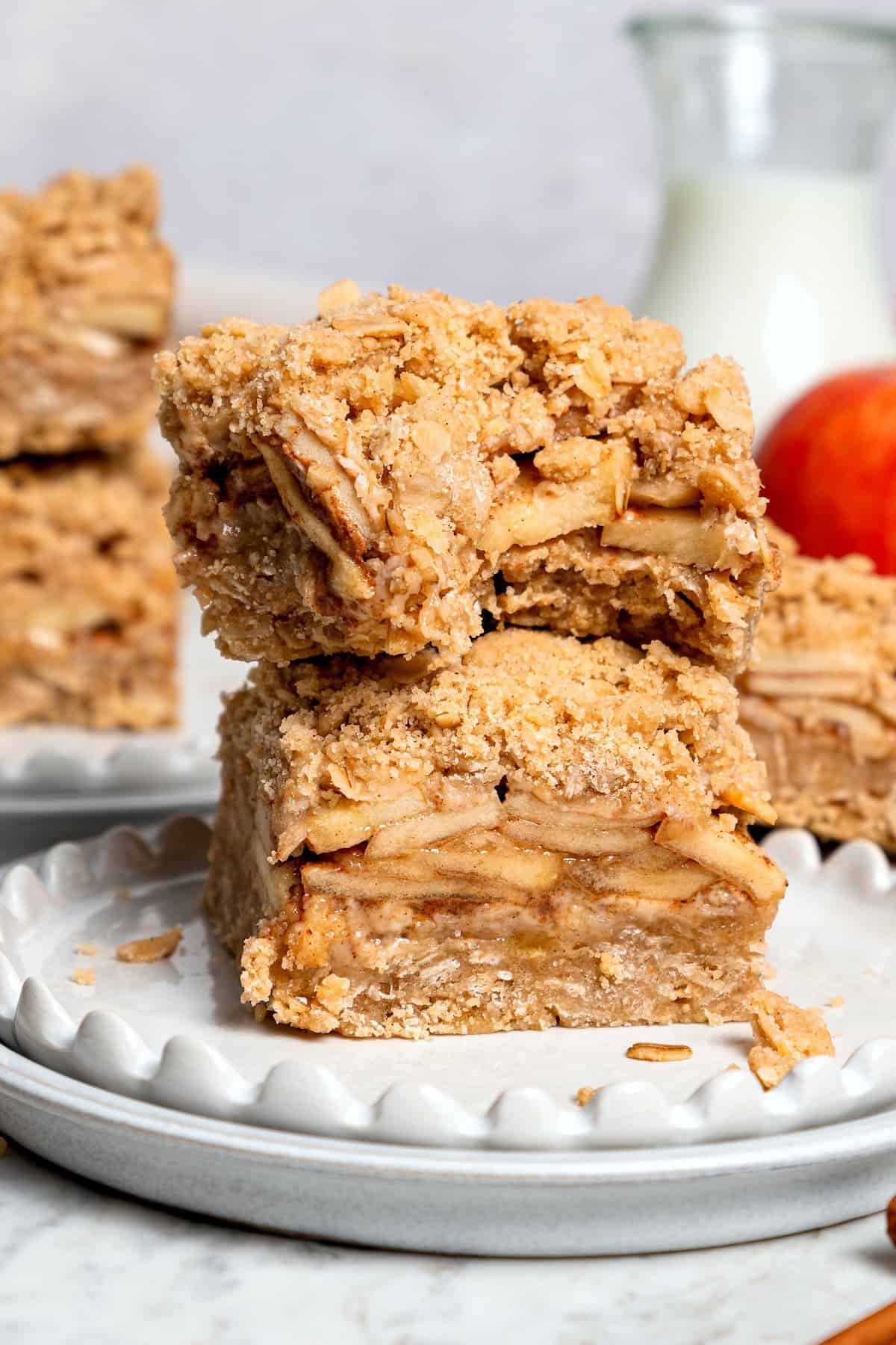 A brown sugar oat crumble mixture doubles as a crust and a topping for these easy Apple Pie Bars. The perfect fall treat for a crowd! Two apple pie bars stacked on plate, with top bar bitten into
