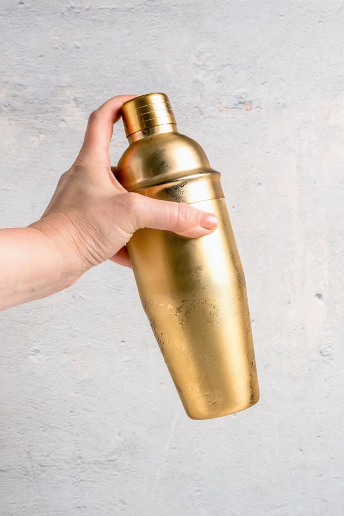 Inspired by the classic dirty martini recipe, pickle brine adds a pop of bold, briny flavor to this savory and smooth pickle martini. Hand holding gold cocktail shaker