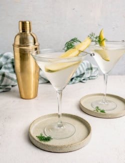 Two dill pickle martinis in glasses garnished with pickle spears and dill