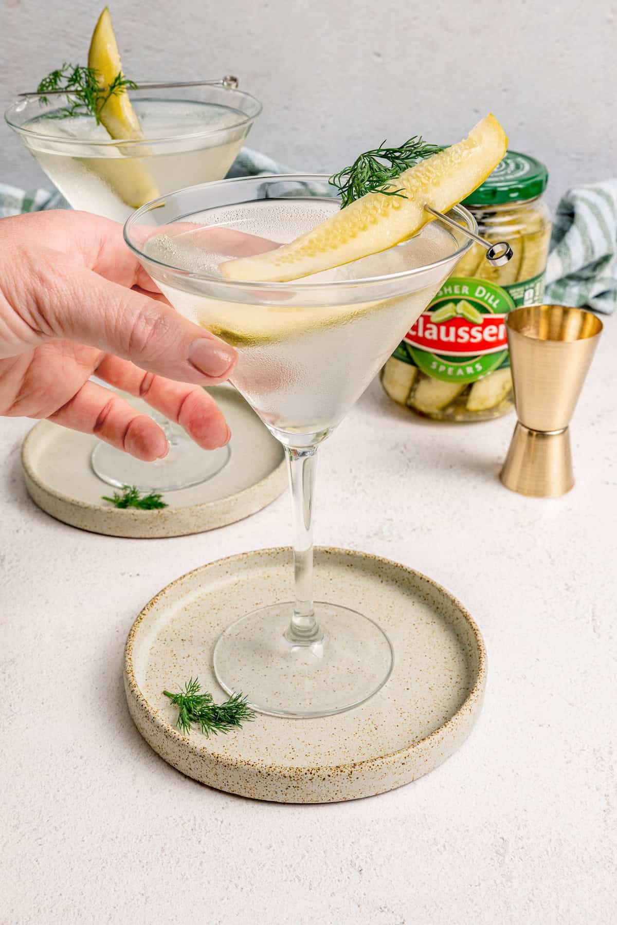 Inspired by the classic dirty martini recipe, pickle brine adds a pop of bold, briny flavor to this savory and smooth pickle martini. Hand reaching for pickle martini in glass