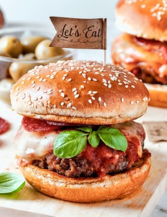 Pizza burgers are served on plates and garnished with basil leaves.