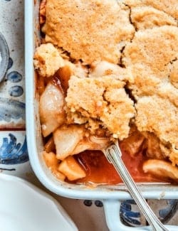a white rectangular baking dish with baked Apple Cobbler, with a spoon removing a portion